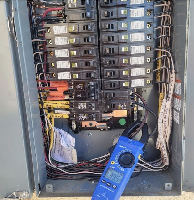 Open residential breaker panel with labeled circuits and a clamp meter taking a reading